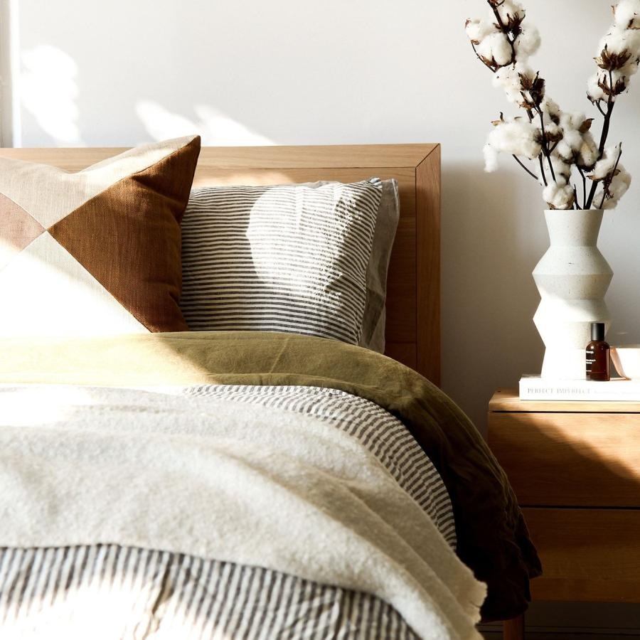 swath of sunlight shines across a well made bed and bedside table with a vase of cotton plants